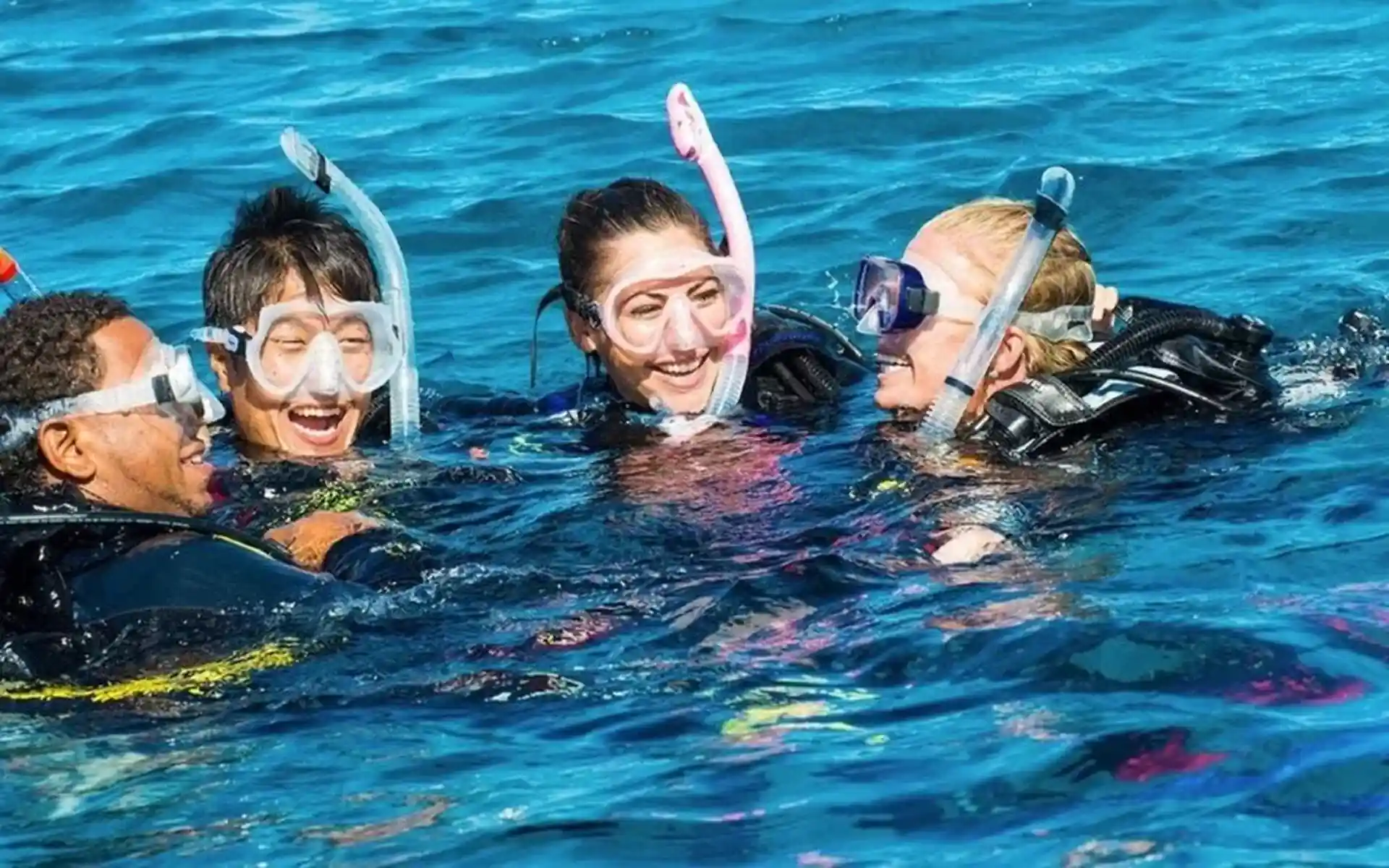 Group of four divers having fun and laughing at the surface before starting their dive