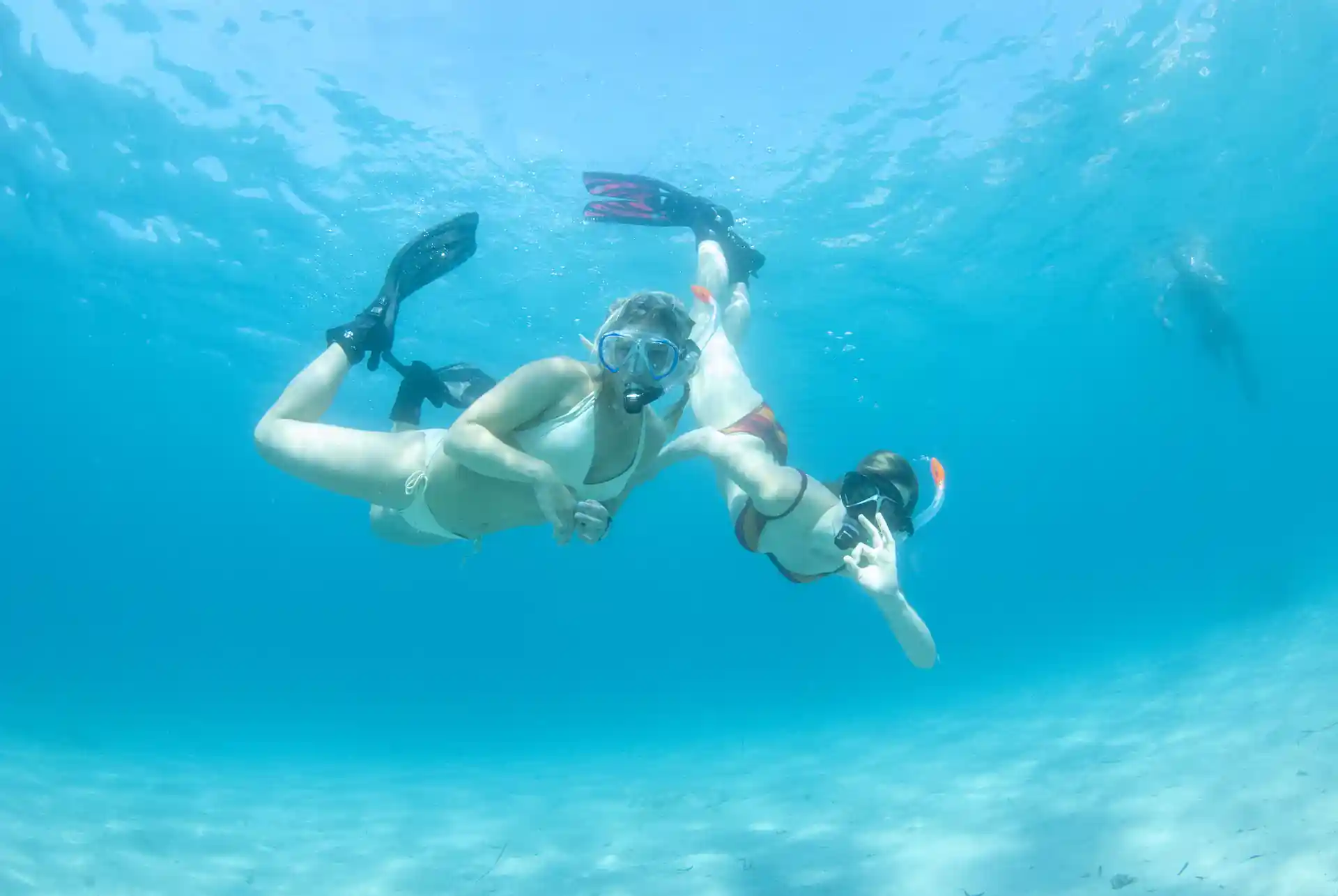 Two young girls snorkeling in crystal-clear waters on a bright summer day.