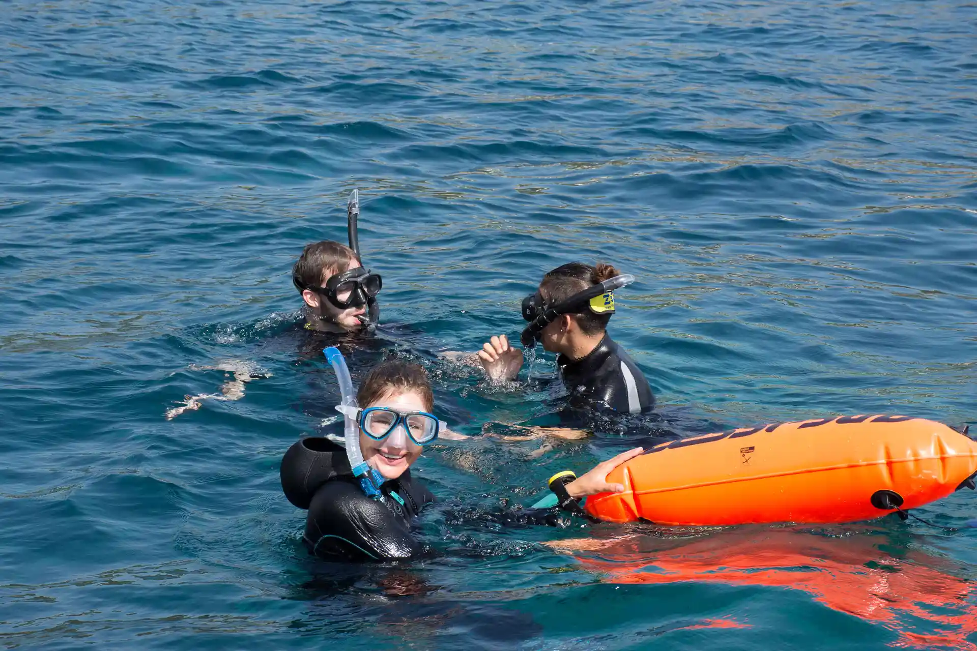 With a buoy trailing behind, a guide leads snorkelers into the clear blue in a protected marine paradise.